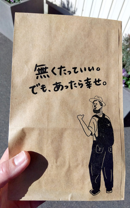 鈴木コーヒーさんの紙袋に書かれた、人の絵と文「無くたっていい。でも、あったら幸せ。」